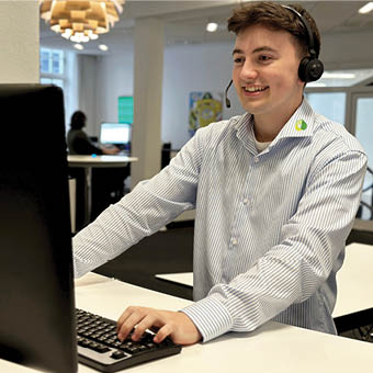 手机和电脑上的 Desk Control™ 应用程序，微笑的ipnordic 员工站立在坐站结合升降桌前