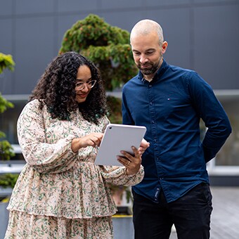 两名 LINAK 员工站在外面，看着 LINAK 大楼前面的平板电脑。