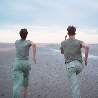 从后面看到的年轻男子和年轻女子，穿着绿色衣服在沙滩上跑。