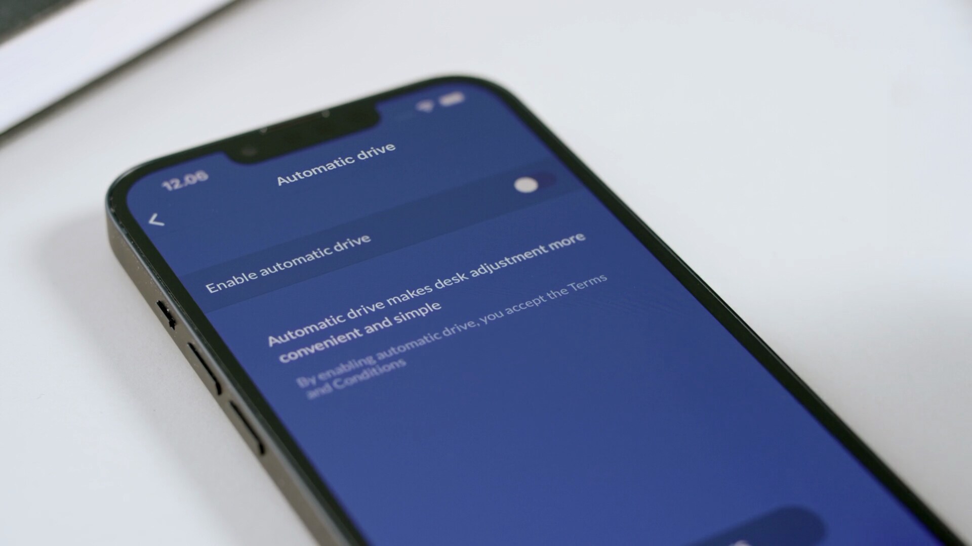 办公桌上的移动设备显示如何通过 Desk Connect™ App 启用 LINAK DPI1C 桌面板的自动驱动屏幕。